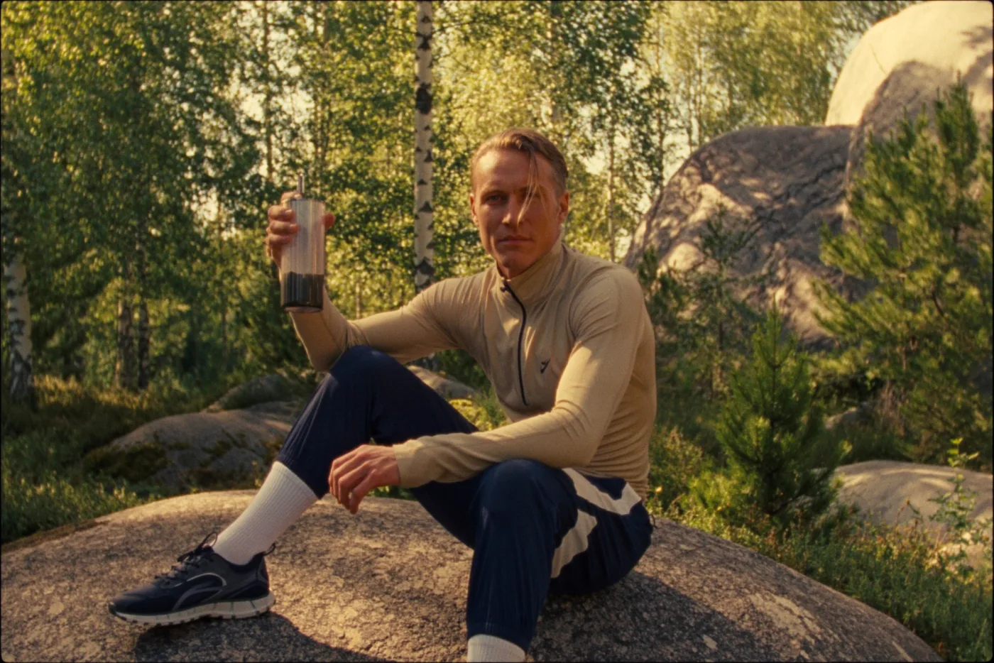 A man seated on a rock in the forest raising a glass of cacao