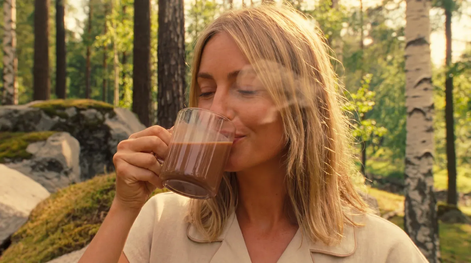 A woman in the forest breathing in the warmth of a cup of cacao held in both hands