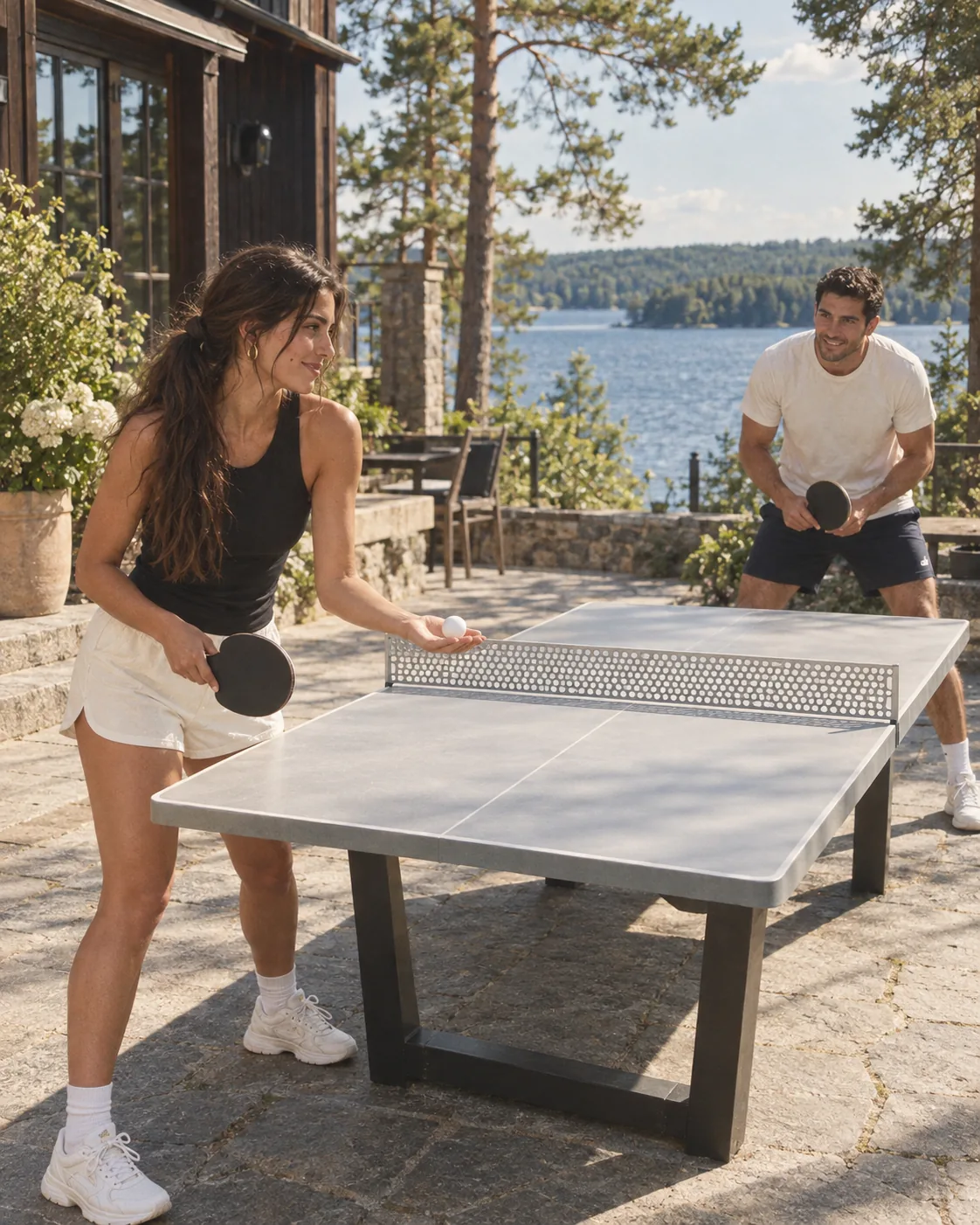 Two people mid rally at a table tennis table on a sunny lakeside terrace