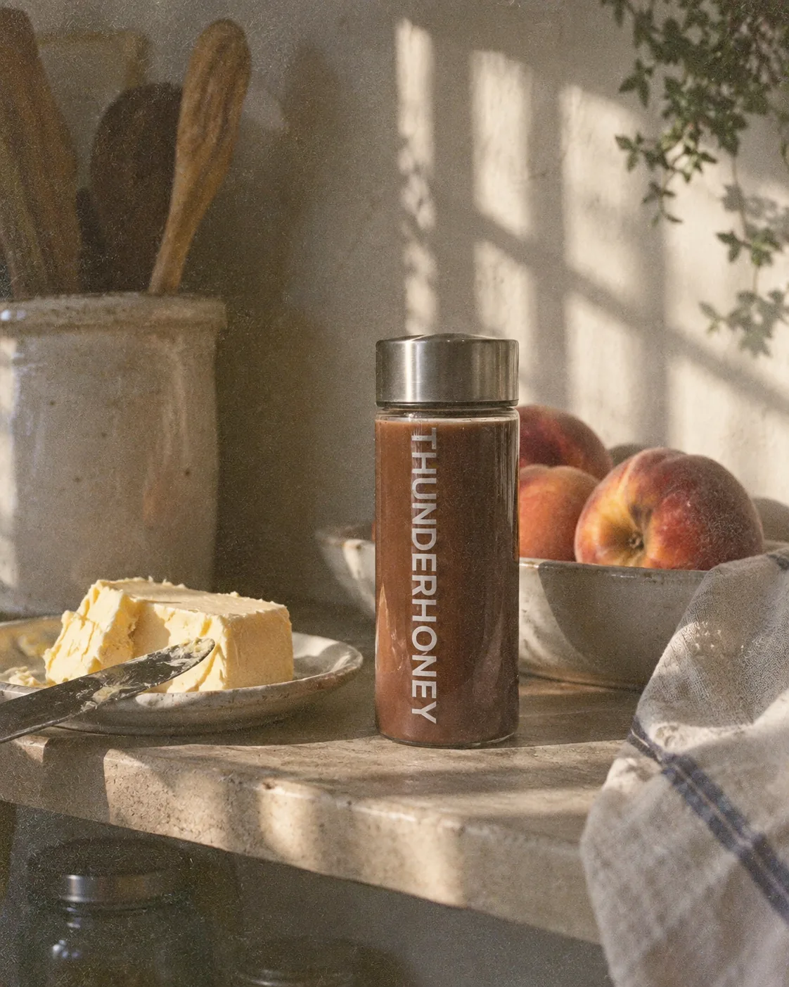 A Thunder Honey bottle on a sunlit kitchen counter beside a bowl of peaches and a dish of butter