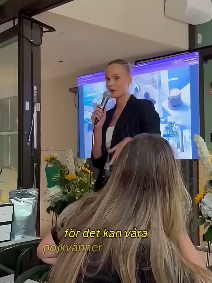 Nina Strauss speaking into a microphone to a seated audience, Thunder Honey pouches on the table beside her