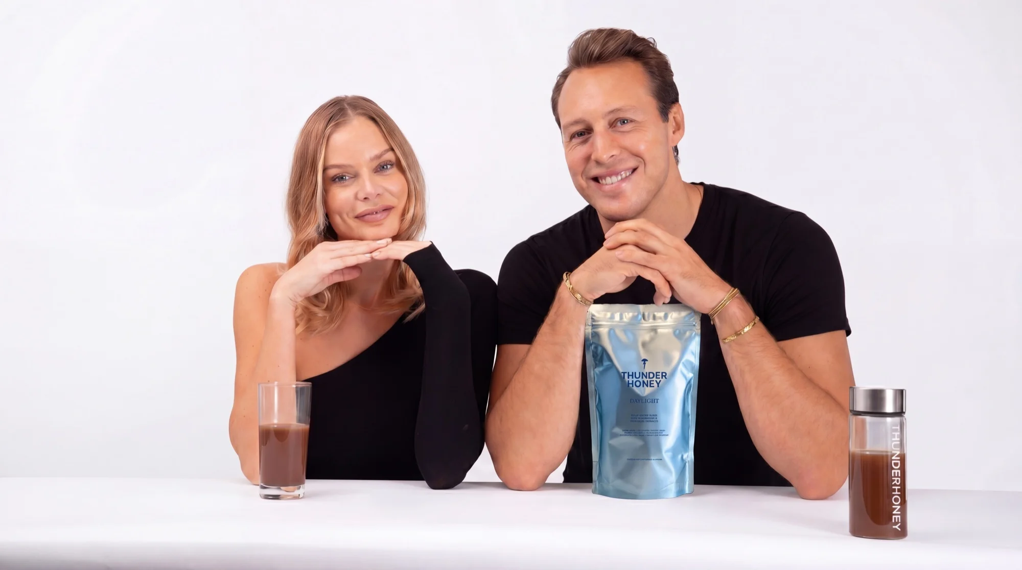The two founders at a white table with the silver Thunder Honey Daylight pouch, a glass of the drink and the glass bottle